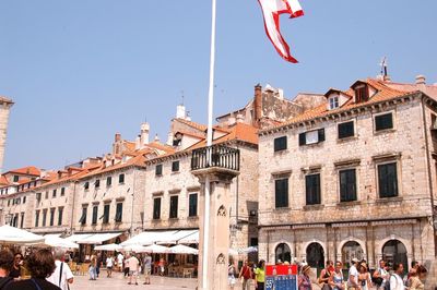 Crowd by buildings against clear sky on sunny day