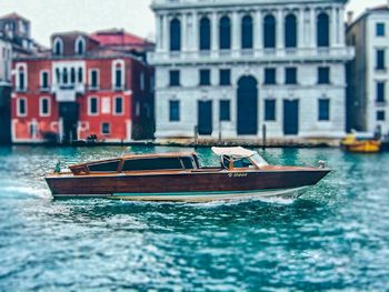 Boat sailing in canal by buildings in city