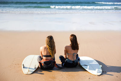 Rear view of female friends sitting at beach