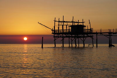 Silhouette built structure in sea against sunset sky