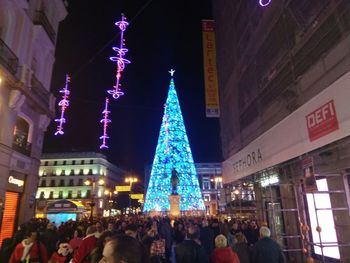 Crowd at illuminated christmas tree against sky at night