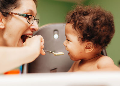 Laughing mother feeding son at home