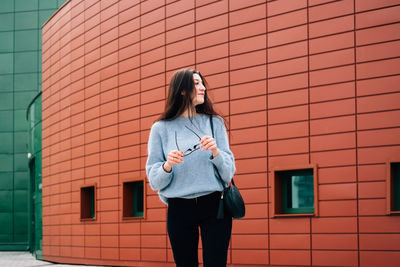 Full length of young woman standing against brick wall