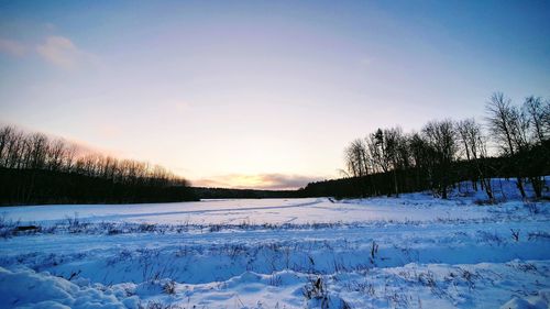 Snow covered field against sky during sunset