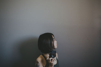 Woman holding camera while standing by wall