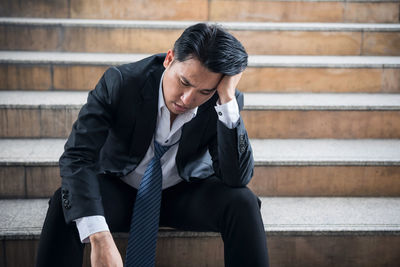 Businessman with headache sitting on steps in city