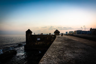 Buildings by sea against sky during sunset in city