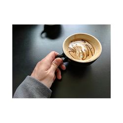 Close-up of hand holding coffee cup on table