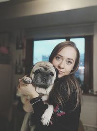 Portrait of young woman holding dog at home