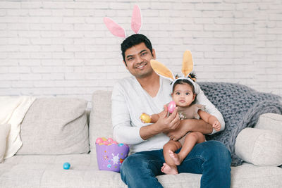 Portrait of smiling mother and daughter sitting on sofa at home