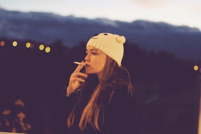 Young woman smoking cigarette against mountains at night