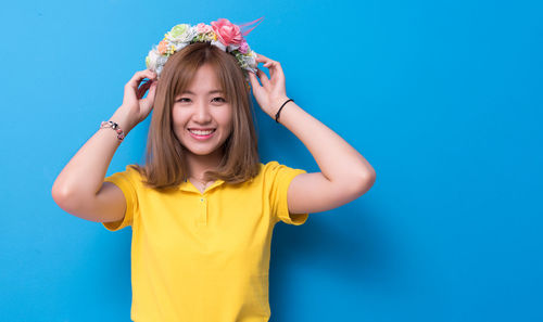 Portrait of beautiful woman wearing flowers against blue background