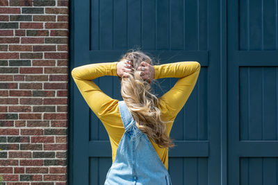 Rear view of woman with hand in hair standing against door