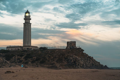 Lighthouse by sea against sky during sunset