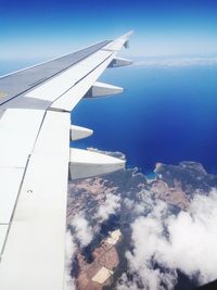 Aerial view of aircraft wing over landscape against blue sky