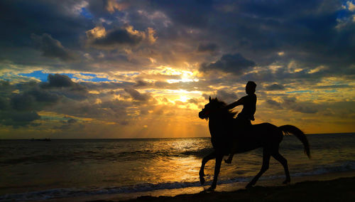 Silhouette man on beach against sky during sunset