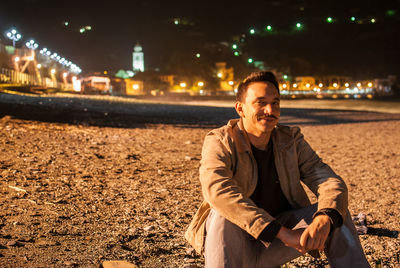 Portrait of man smiling while sitting at illuminated beach