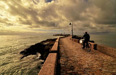 Man riding bicycle on beach against sky during sunset