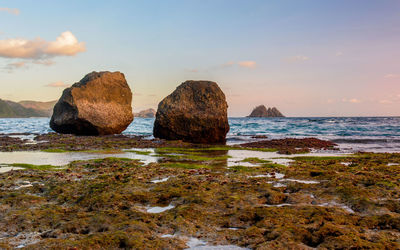 Rocks on beach against sky during sunset