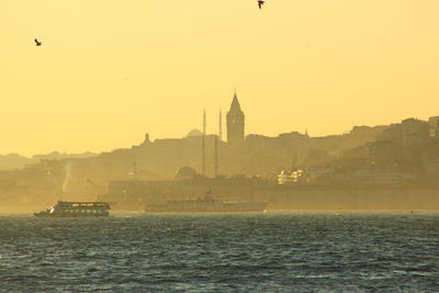 Passenger crafts sailing in strait by galata tower against clear sky during sunset