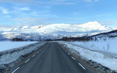 Snow covered road by snowcapped mountain against sky