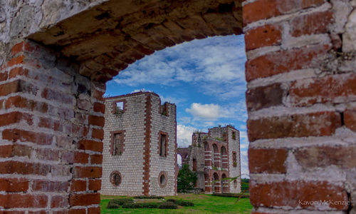 Buildings against sky seen through brick wall