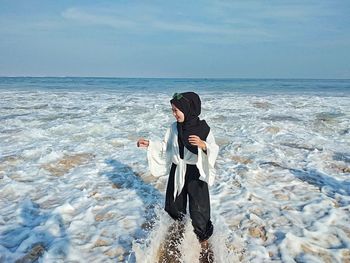 Rear view of woman standing at beach against sky