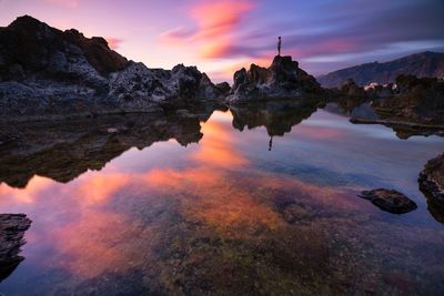 Scenic view of lake by rock formation against sky during sunset