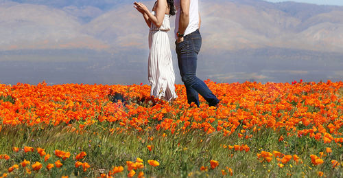 Woman standing by flowering plants on field against sky