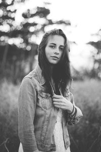 Portrait of young woman standing on grassy field against sky