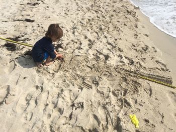 High angle view of boy playing with sand at beach during sunny day