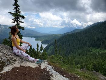 Side view of man sitting on mountain against sky