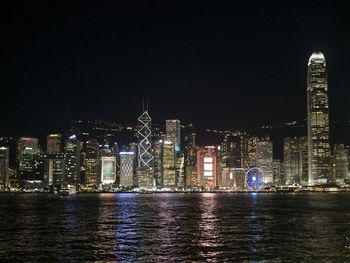 Illuminated city by river against sky at night