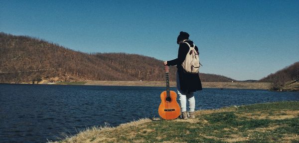 Rear view of woman standing by lake against sky