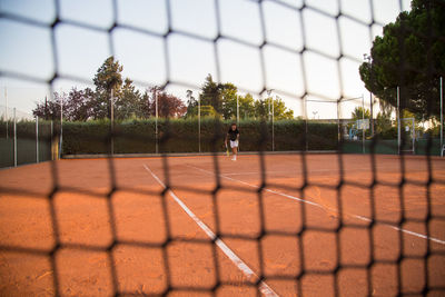 Man playing tennis on court seen through net