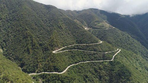 Mountain curve is road passing along the slopes of mountains and hills covered with green forest 