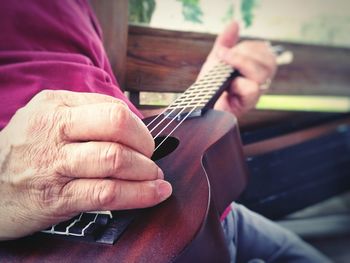 Midsection of man playing guitar while sitting on bench