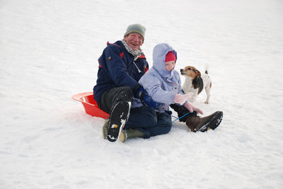 Father and son with dog sitting on snow field