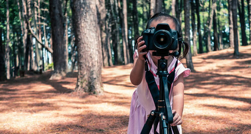 Girl photographing against trees in forest