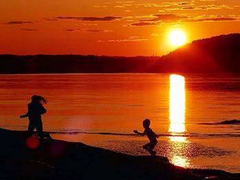 Silhouette people on beach against orange sky