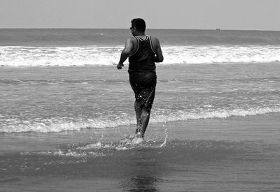 Rear view of man running at beach against sky