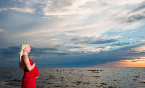 Pregnant woman standing in front of baltic sea against cloudy sky