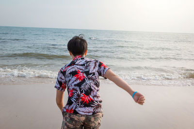 Rear view of boy on beach against sky