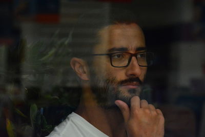 Close-up of thoughtful man wearing eyeglasses seen through window