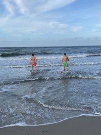 Rear view of people on beach against sky