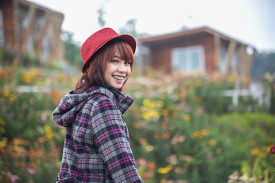 Portrait of young woman wearing hat standing by plants against sky