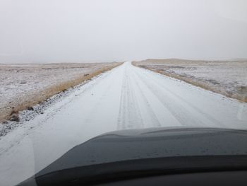 Snow covered country road against clear sky seen from car windshield