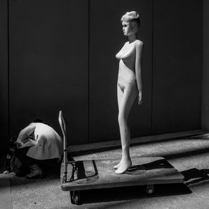 Rear view of person crouching by mannequin on push cart against wall