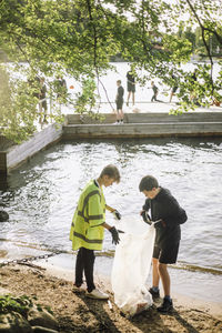 Full length of boys with garbage bag at lakeshore