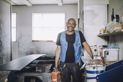 Portrait of smiling bald painter standing by workbench at workshop